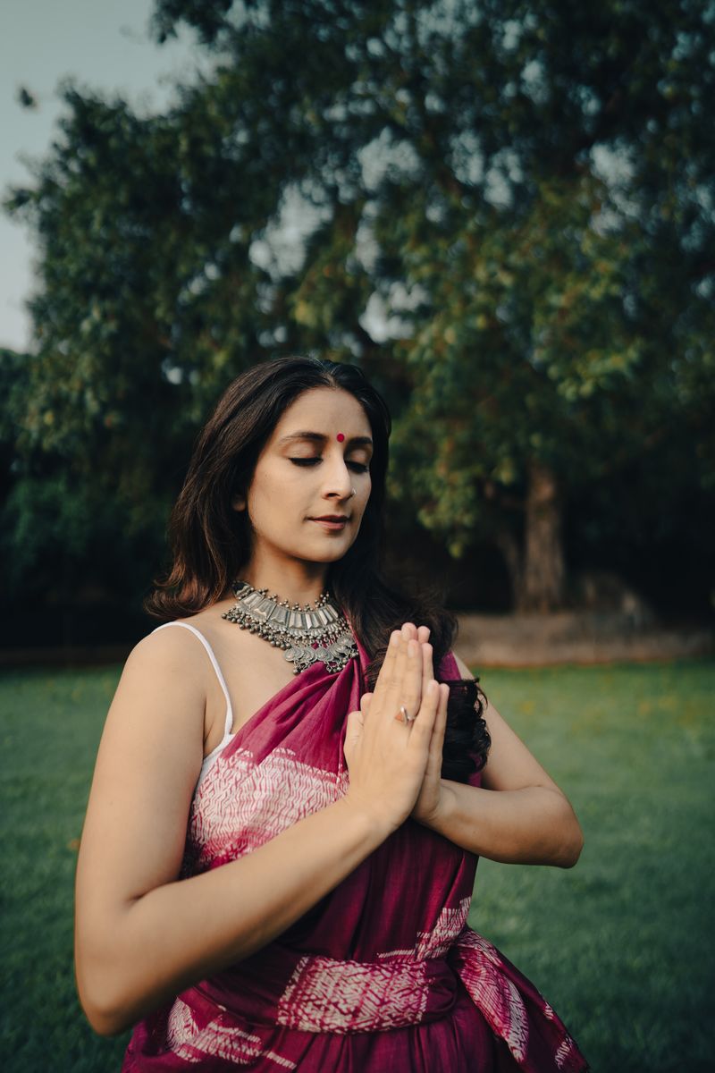Shikha with her palms together, eyes closed, under a tree