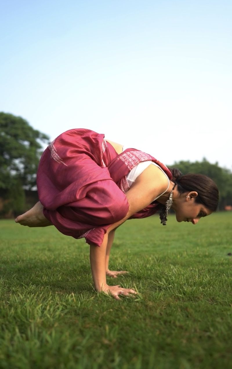 Shikha holding crow pose on a lawn
