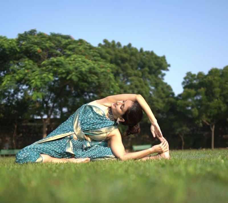 Shikha in a seated side stretch on a lawn, in a teal sari