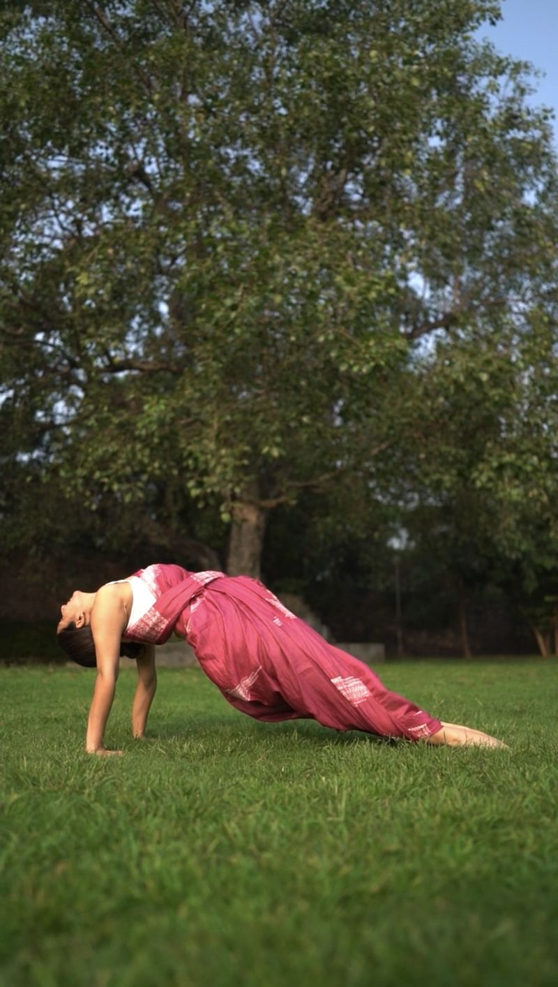 Shikha in reverse plank on a lawn, under a large tree